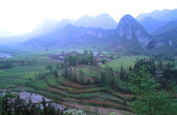 Extrémité de la vallée aveugle de la Yunihe. La rivière se perd quelques centaines de mètres en amont (à gauche de la photo). Au centre le superbe village de Zhongyin et à droite le porche fossile de Yangjiayandong correspondant à l’ancienne perte de la Yunihe. End of the blind valley of Yunihe. In the center, the beautiful village of Zhongyin, on the right the dry entrance of Yangjiadong, the former sinkhole of Yunihe. (Panxian Guizhou)