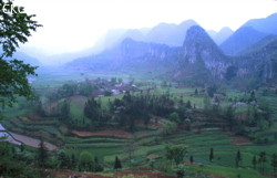 Extrémité de la vallée aveugle de la Yunihe. La rivière se perd quelques centaines de mètres en amont (à gauche de la photo). Au centre le superbe village de Zhongyin et à droite le porche fossile de Yangjiayandong correspondant à l’ancienne perte de la Yunihe. End of the blind valley of Yunihe. In the center, the beautiful village of Zhongyin, on the right the dry entrance of Yangjiadong, the former sinkhole of Yunihe. (Panxian Guizhou)