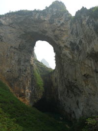 Dans la paroi est de l'énorme effondrement (un Tiankeng de pente dégénéré) de 200 m de diamètre, un gros porche perché forme un pont-naturel. Il domine plan d'eau regard sur la rivière souterraine. Grotte de Dajing dong Qun 大井洞. (Dajing 大井, Qiannan 黔南, Luodian罗甸, Guizhou 贵州省, Chine)