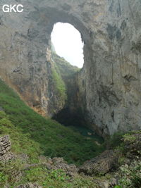 Dans la paroi est de l'énorme effondrement (un Tiankeng de pente dégénéré) de 200 m de diamètre, un gros porche perché forme un pont-naturel. Il domine plan d'eau regard sur la rivière souterraine. Grotte de Dajing dong Qun 大井洞. (Dajing 大井, Qiannan 黔南, Luodian罗甸, Guizhou 贵州省, Chine)