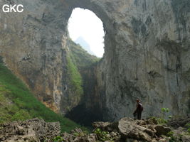 Dans la paroi est de l'énorme effondrement (un Tiankeng de pente dégénéré) de 200 m de diamètre, un gros porche perché forme un pont-naturel. Il domine plan d'eau regard sur la rivière souterraine. Grotte de Dajing dong Qun 大井洞. (Dajing 大井, Qiannan 黔南, Luodian罗甸, Guizhou 贵州省, Chine)