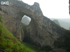 Dans la paroi est de l'énorme effondrement (un Tiankeng de pente dégénéré) de 200 m de diamètre, un gros porche perché forme un pont-naturel. Il domine plan d'eau regard sur la rivière souterraine. Grotte de Dajing dong Qun 大井洞. (Dajing 大井, Qiannan 黔南, Luodian罗甸, Guizhou 贵州省, Chine)