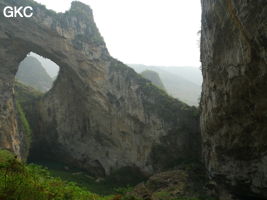 Dans la paroi est de l'énorme effondrement (un Tiankeng de pente dégénéré) de 200 m de diamètre, un gros porche perché forme un pont-naturel. Il domine plan d'eau regard sur la rivière souterraine. Grotte de Dajing dong Qun 大井洞. (Dajing 大井, Qiannan 黔南, Luodian罗甸, Guizhou 贵州省, Chine)