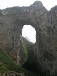 Dans la paroi est de l'énorme effondrement (un Tiankeng de pente dégénéré) de 200 m de diamètre, un gros porche perché forme un pont-naturel. Il domine plan d'eau regard sur la rivière souterraine. Grotte de Dajing dong Qun 大井洞. (Dajing 大井, Qiannan 黔南, Luodian罗甸, Guizhou 贵州省, Chine)