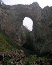 Dans la paroi est de l'énorme effondrement (un Tiankeng de pente dégénéré) de 200 m de diamètre, un gros porche perché forme un pont-naturel. Il domine plan d'eau regard sur la rivière souterraine. Grotte de Dajing dong Qun 大井洞. (Dajing 大井, Qiannan 黔南, Luodian罗甸, Guizhou 贵州省, Chine)