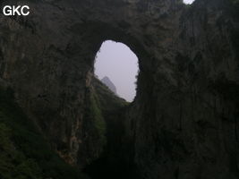 Dans la paroi est de l'énorme effondrement (un Tiankeng de pente dégénéré) de 200 m de diamètre, un gros porche perché forme un pont-naturel. Grotte de Dajing dong Qun 大井洞. (Dajing 大井, Qiannan 黔南, Luodian罗甸, Guizhou 贵州省, Chine)