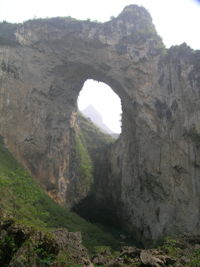 Dans la paroi est de l'énorme effondrement (un Tiankeng de pente dégénéré) de 200 m de diamètre, un gros porche perché forme un pont-naturel. Il domine plan d'eau regard sur la rivière souterraine. Grotte de Dajing dong Qun 大井洞. (Dajing 大井, Qiannan 黔南, Luodian罗甸, Guizhou 贵州省, Chine)