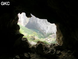 Dans l'énorme effondrement (un Tiankeng de pente dégénéré) de 200 m de diamètre. Vu d'une des grottes abri de la paroi ouest : le plan d'eau regard sur la rivière souterraine, occupe le coin est. Grotte de Dajing dong Qun 大井洞. (Dajing 大井, Qiannan 黔南, Luodian罗甸, Guizhou 贵州省, Chine)