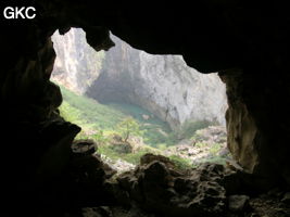 Dans l'énorme effondrement (un Tiankeng de pente dégénéré) de 200 m de diamètre. Vu d'une des grottes abri de la paroi ouest : le plan d'eau regard sur la rivière souterraine, occupe le coin est. Grotte de Dajing dong Qun 大井洞. (Dajing 大井, Qiannan 黔南, Luodian罗甸, Guizhou 贵州省, Chine)