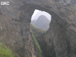 Dans la paroi est de l'énorme effondrement (un Tiankeng de pente dégénéré) de 200 m de diamètre, un gros porche perché forme un pont-naturel. Grotte de Dajing dong Qun 大井洞. (Dajing 大井, Qiannan 黔南, Luodian罗甸, Guizhou 贵州省, Chine)