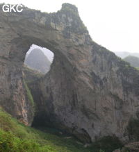 Dans la paroi est de l'énorme effondrement (un Tiankeng de pente dégénéré) de 200 m de diamètre, un gros porche perché forme un pont-naturel. Il domine plan d'eau regard sur la rivière souterraine. Grotte de Dajing dong Qun 大井洞. (Dajing 大井, Qiannan 黔南, Luodian罗甸, Guizhou 贵州省, Chine)