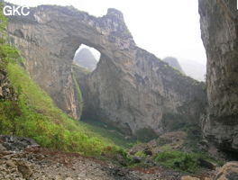 Dans la paroi est de l'énorme effondrement (un Tiankeng de pente dégénéré) de 200 m de diamètre, un gros porche perché forme un pont-naturel. Il domine plan d'eau regard sur la rivière souterraine. Grotte de Dajing dong Qun 大井洞. (Dajing 大井, Qiannan 黔南, Luodian罗甸, Guizhou 贵州省, Chine)