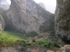 Dans l'énorme effondrement (un Tiankeng de pente dégénéré) de 200 m de diamètre. Un plan d'eau, occupe le coin est,  il correspond à un regard sur la résurgence, comme l'indique un lent mouvement tourbillonnaire. De nombreux indices sont la preuve d'importantes fluctuations de la nappe, notamment un niveau bien marqué sur la paroi, à plus de cinq mètres au-dessus du plan d'eau. Grotte de Dajing dong Qun 大井洞. (Dajing 大井, Qiannan 黔南, Luodian罗甸, Guizhou 贵州省, Chine)