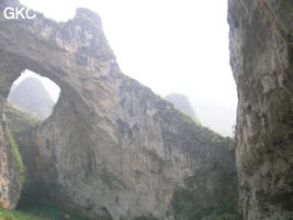 Dans la paroi est de l'énorme effondrement (un Tiankeng de pente dégénéré) de 200 m de diamètre, un gros porche perché forme un pont-naturel. Il domine plan d'eau regard sur la rivière souterraine. Grotte de Dajing dong Qun 大井洞. (Dajing 大井, Qiannan 黔南, Luodian罗甸, Guizhou 贵州省, Chine)